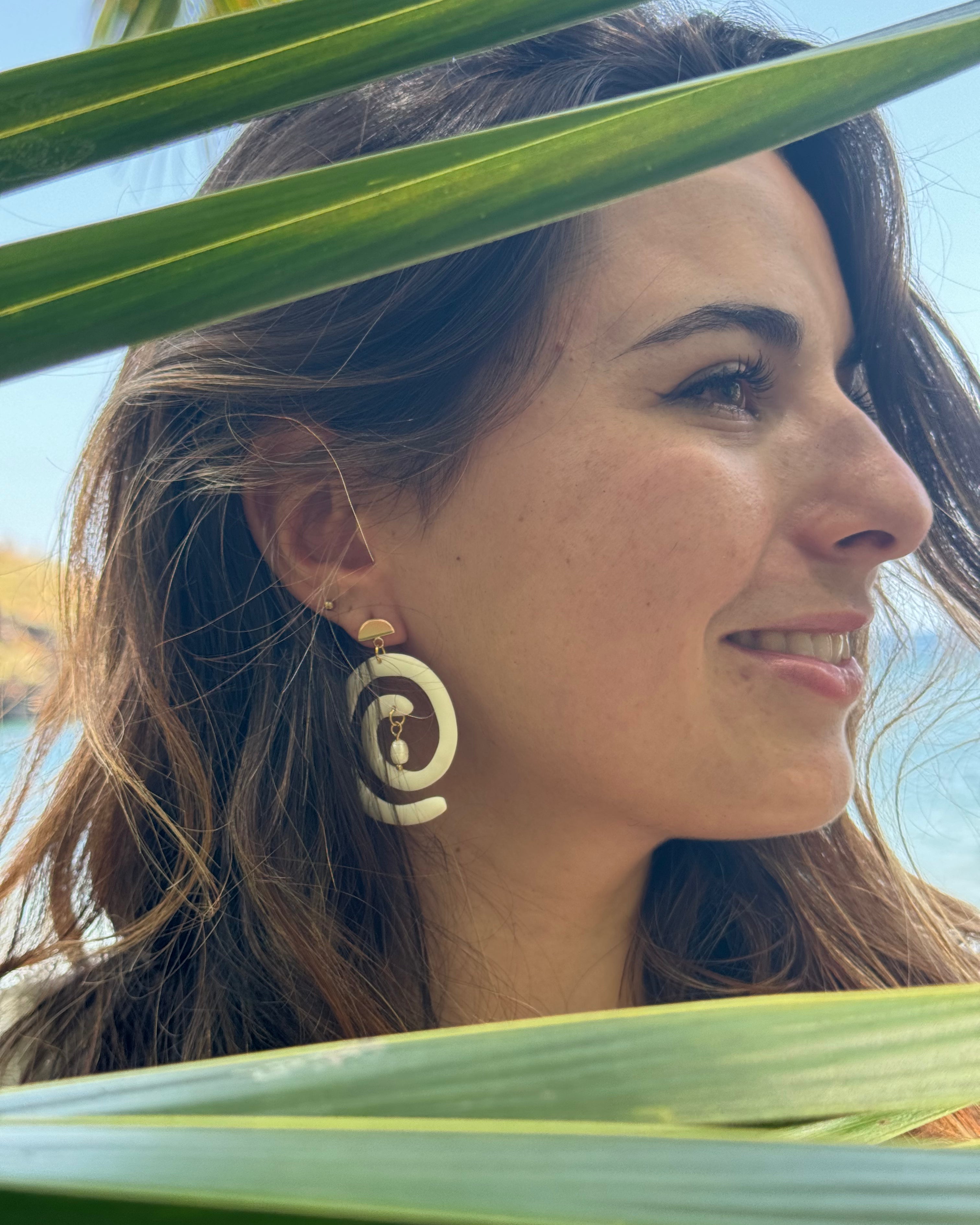 boucles d'oreilles en forme de spirale blanches, avec une attache en plaqué or. Une perle d'eau douce fabriquée à la main en argile polymère pend au centre de la spirale. Design moderne et chic.